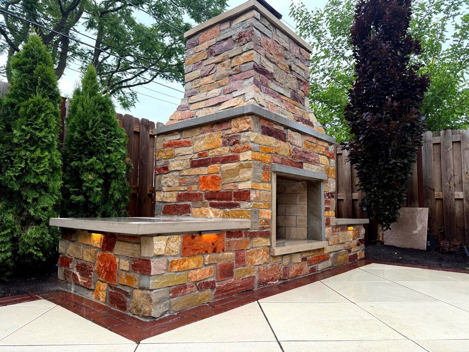 Custom multi-color stone outdoor fireplace with a concrete hearth and seating ledge built by Topo d'Oro Landscape Design